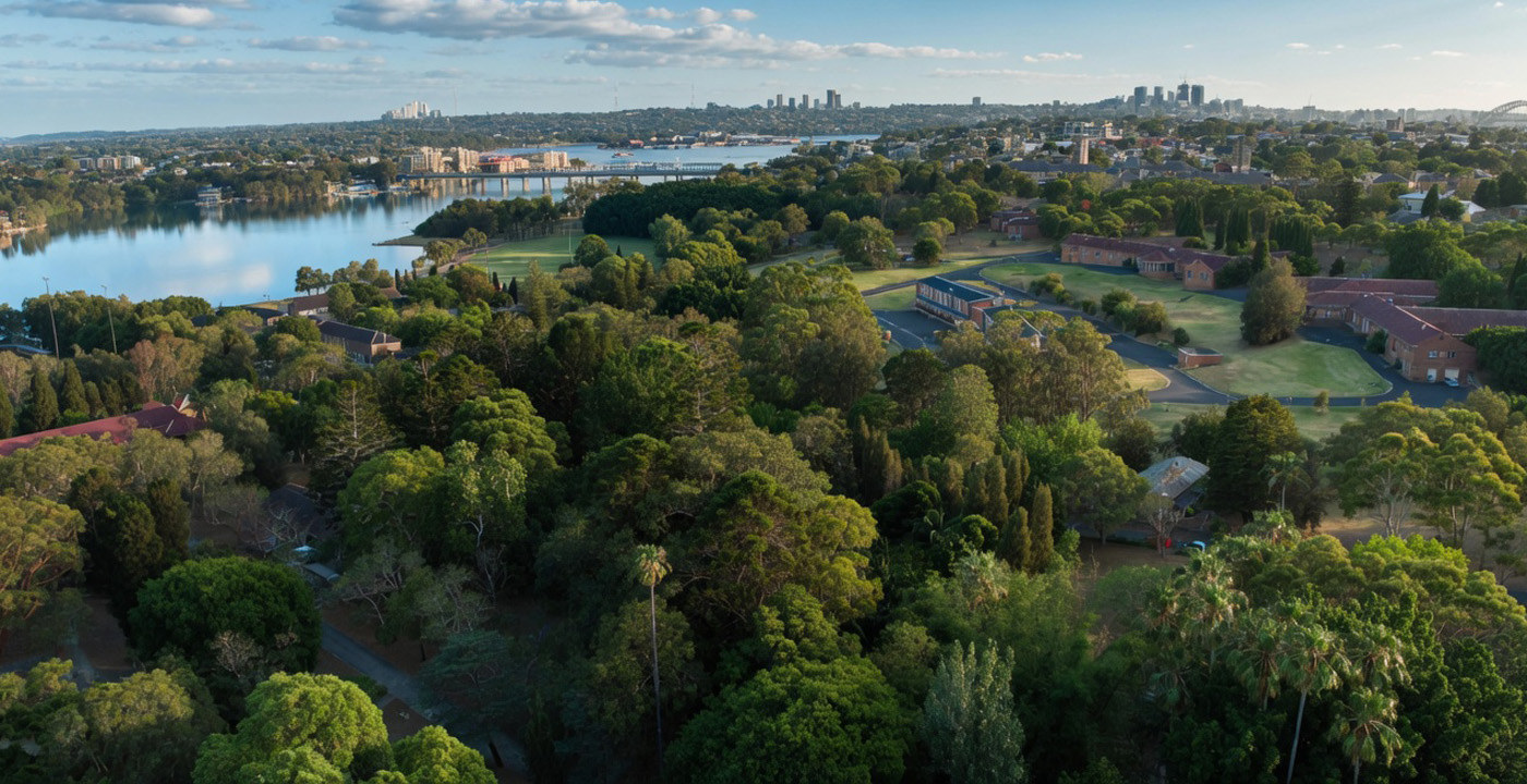 Aerial view over the parklands at the WHOS Lilyfield campus, looking across the water to the Sydney skyline