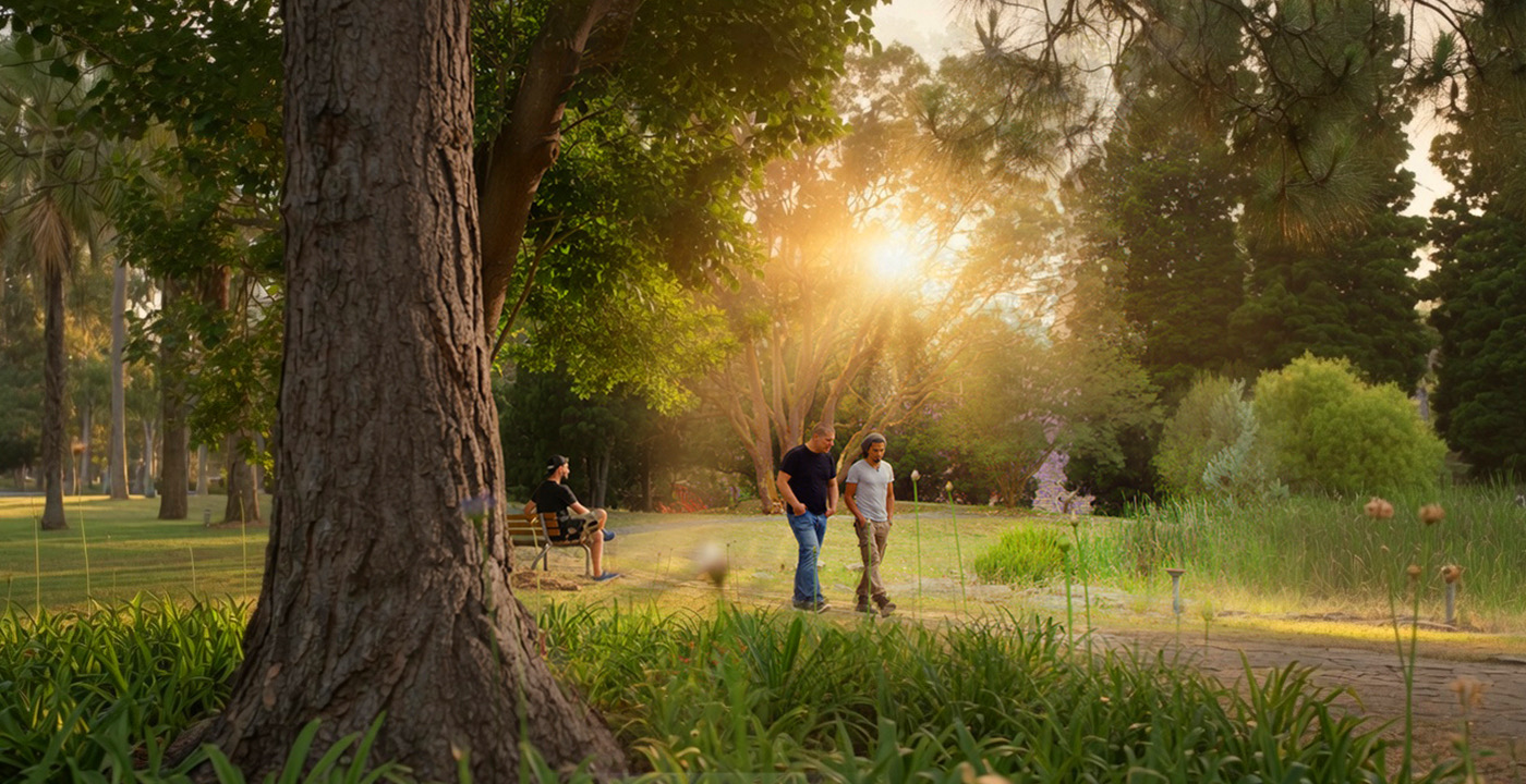 Two men walking through sunlit parkland at a WHOS residential site.