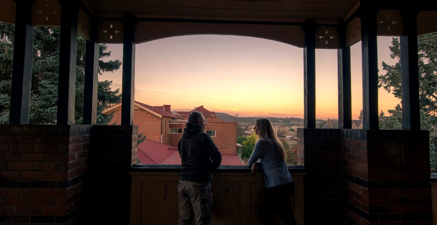 Two people talking together on a veranda at sunset.